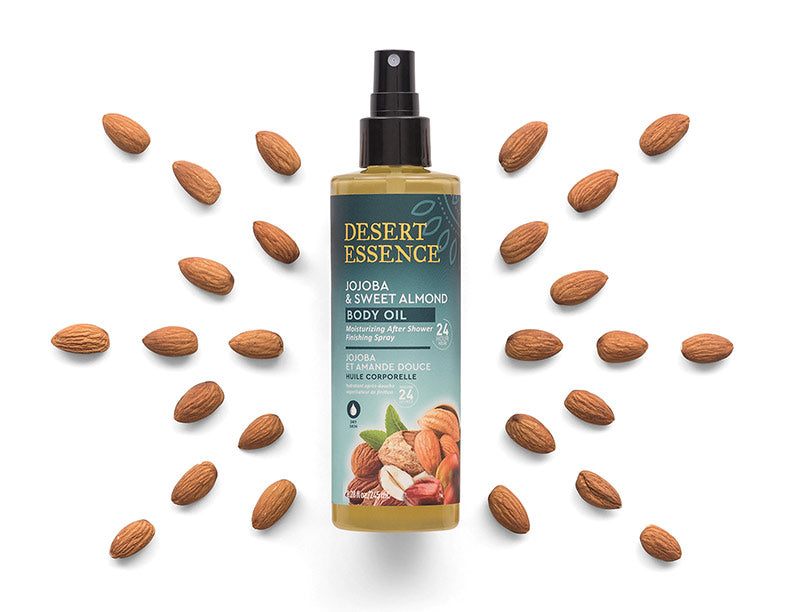 Bottle of Desert Essence jojoba and sweet almond body oil on white background with almonds.
