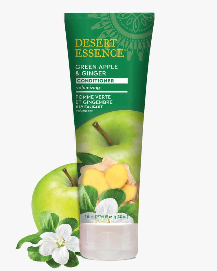 Tube of Desert Essence Green Apple and Ginger Conditioner, volumizing formula, 8 fl. oz next to a green apple and flower..