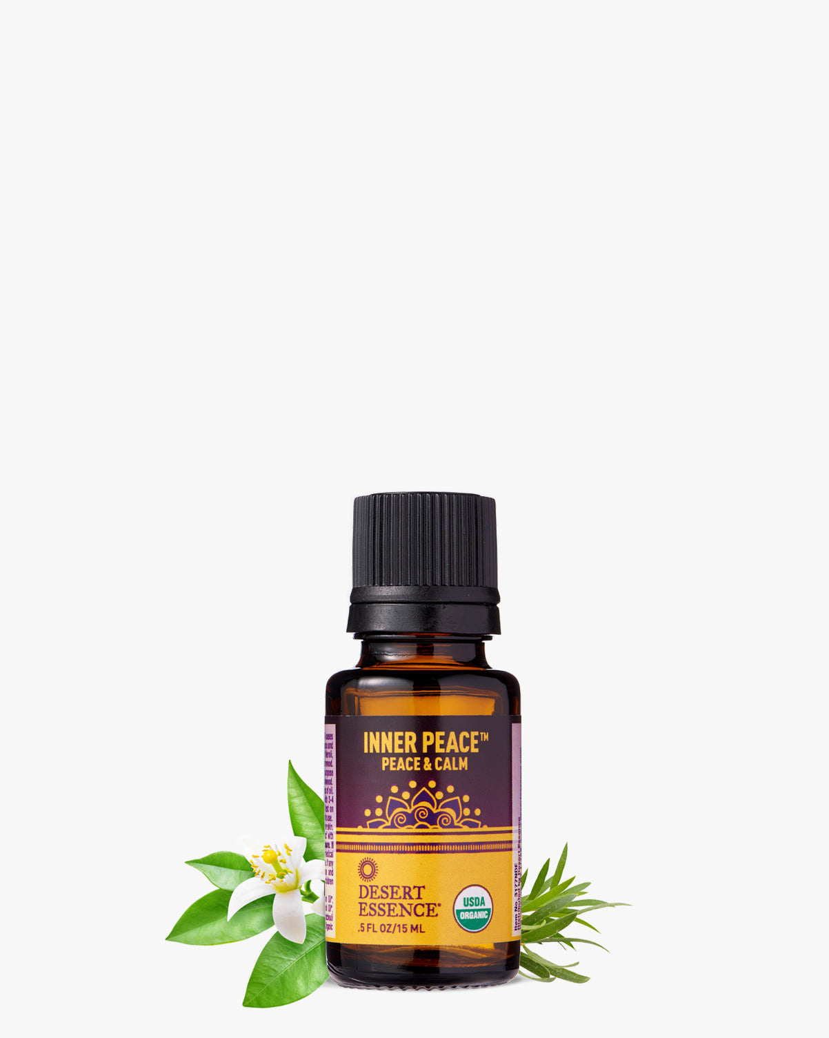 Inner Peace Organic Essential Oil bottle with amber glass and black cap, displayed alongside fresh green leaves and white flower blossoms. Purple label features golden mandala design on Desert Essence packaging.
