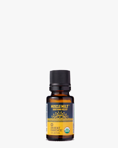 Muscle Melt Organic Essential Oil in amber glass bottle with black cap, featuring gold and navy label design with ornate mandala pattern. Desert Essence branded organic aromatherapy blend for muscle tension relief.