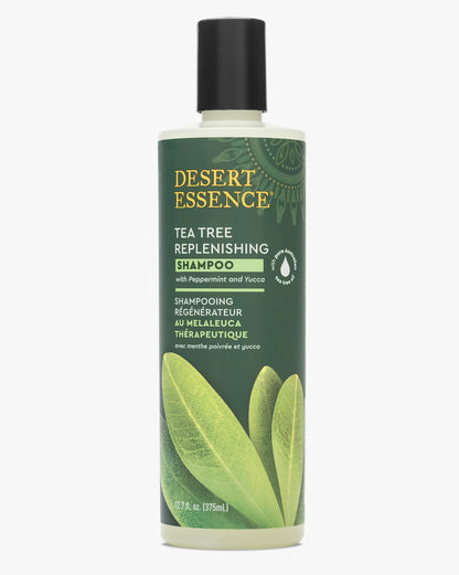 Desert Essence Tea Tree Replenishing Shampoo bottle featuring a green label with gold lettering and botanical leaf design, containing natural tea tree oil and peppermint for scalp health and shine.