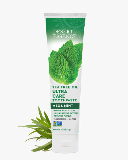 Desert Essence Tea Tree Oil Ultra Care Toothpaste tube with green leaves on a white background