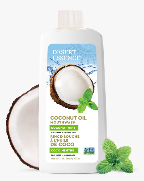 Desert Essence Coconut Oil Mouthwash bottle with a coconut half and mint leaves on a white background