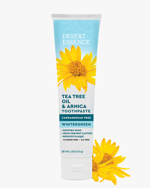 Desert Essence Tea Tree Oil & Arnica Toothpaste tube with sunflower graphics on a white background
