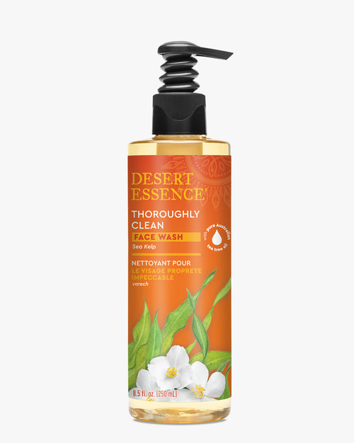 Desert Essence Thoroughly Clean Face Wash with Sea Kelp in a clear bottle with orange label, featuring botanical illustrations of green leaves and white flowers. Black pump dispenser top, showing natural tea tree and sea kelp formula for gentle facial cleansing.