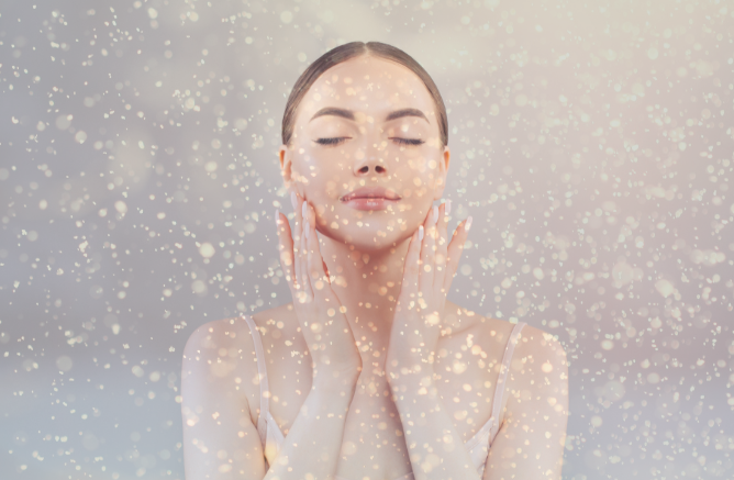 Woman with closed eyes touching her face gently, surrounded by a soft flurry of snowflakes, possibly using one of the top 5 personal care products for winter.