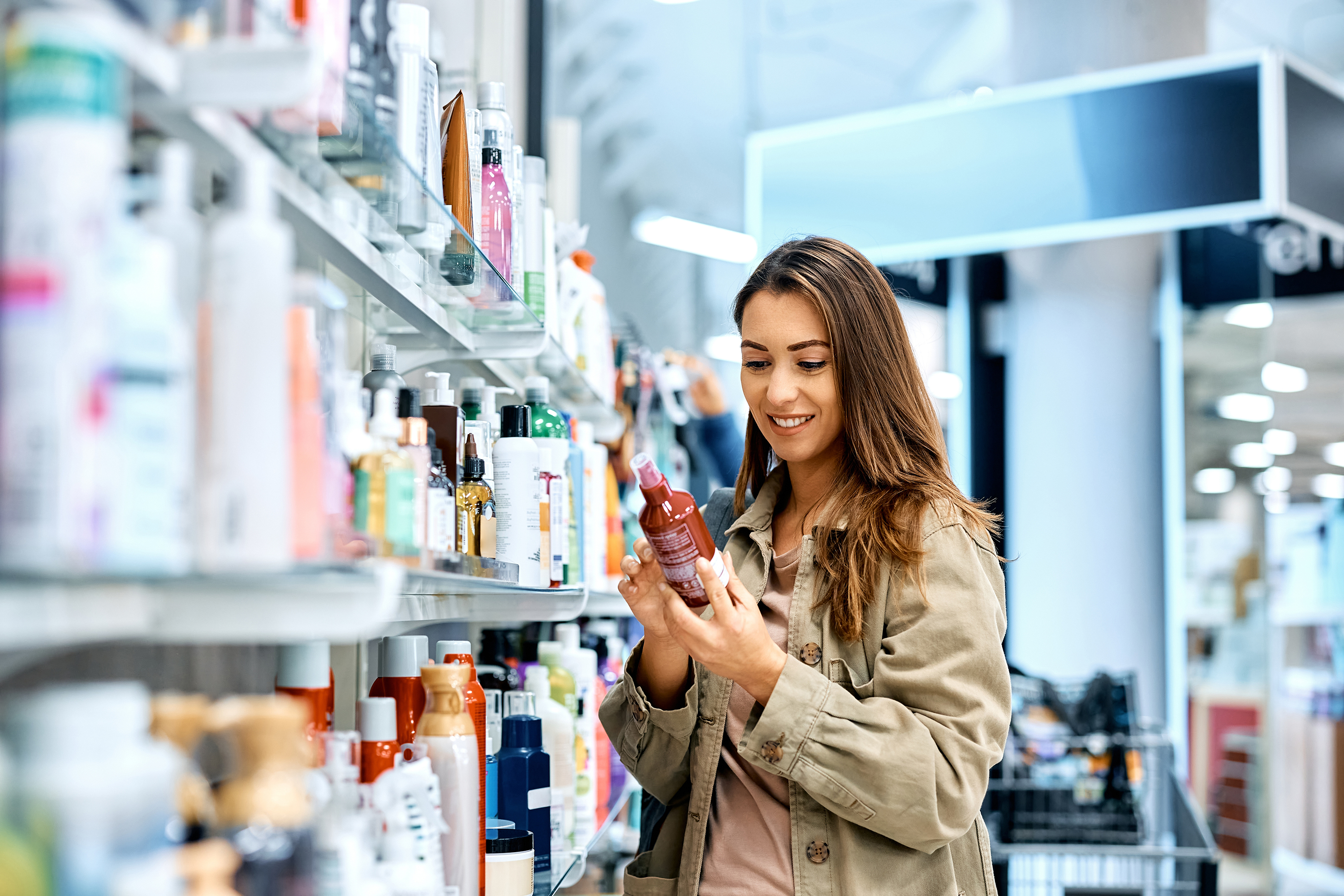 Smiling woman examining a hair product in a store aisle, searching for cruelty-free beauty options.