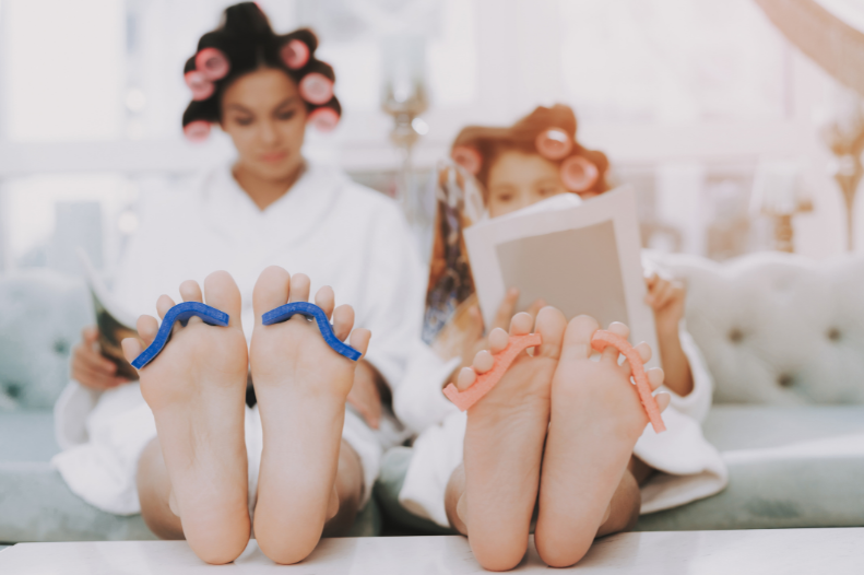 A mother and child in white robes and hair curlers during a pampering session, with focus on Mother's day gift ideas.