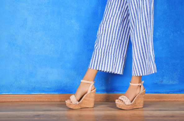 Person wearing striped culottes and beige wedge sandals against a vibrant blue wall.