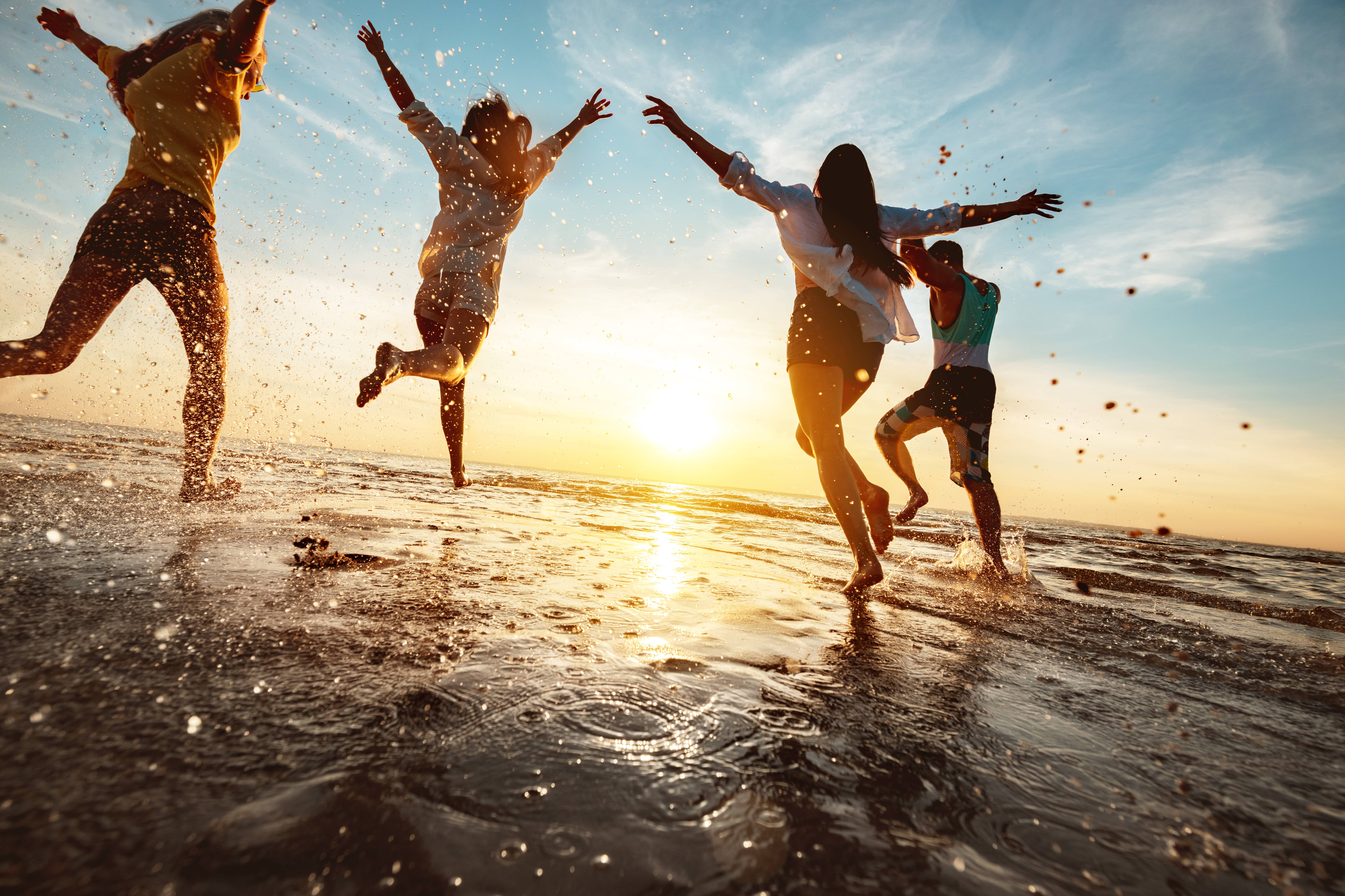 Friends jumping on the beach at sunset, splashing water around, reflecting an active lifestyle in a humid climate suitable for skincare topics.