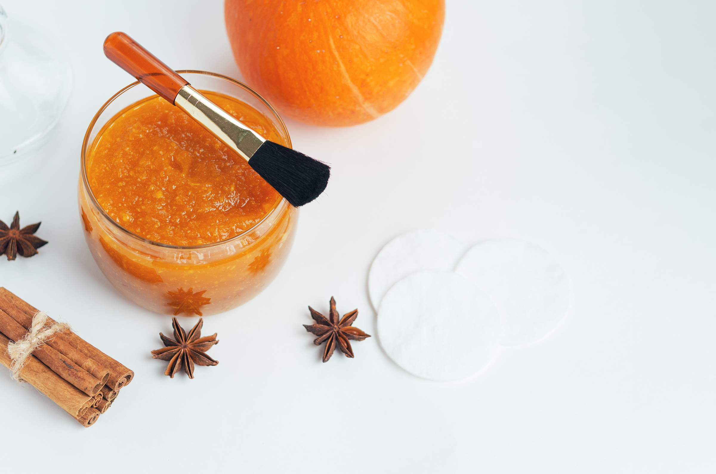 Homemade pumpkin jojoba face mask in a glass jar with a brush, surrounded by cinnamon sticks and star anise, for a fall renewal skincare theme.