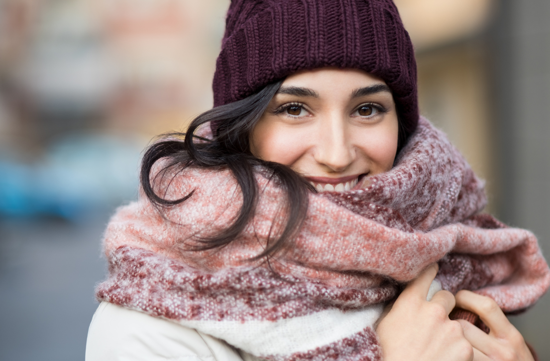 Woman with a joyful smile, bundled up in a winter hat and scarf, seems pleased as she learns about debunked winter skincare myths from Desert Essence.