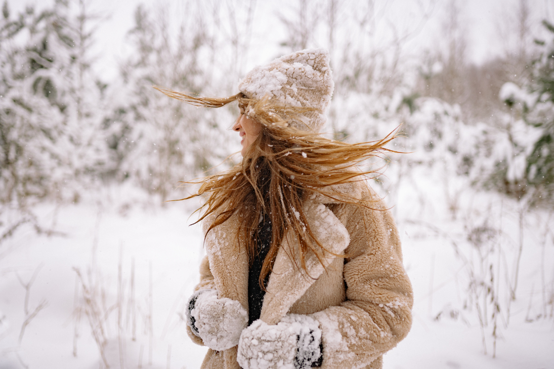 Woman with wind-blown hair in a winter landscape, showing the challenges addressed in the 'Winter Hair Survival Guide."