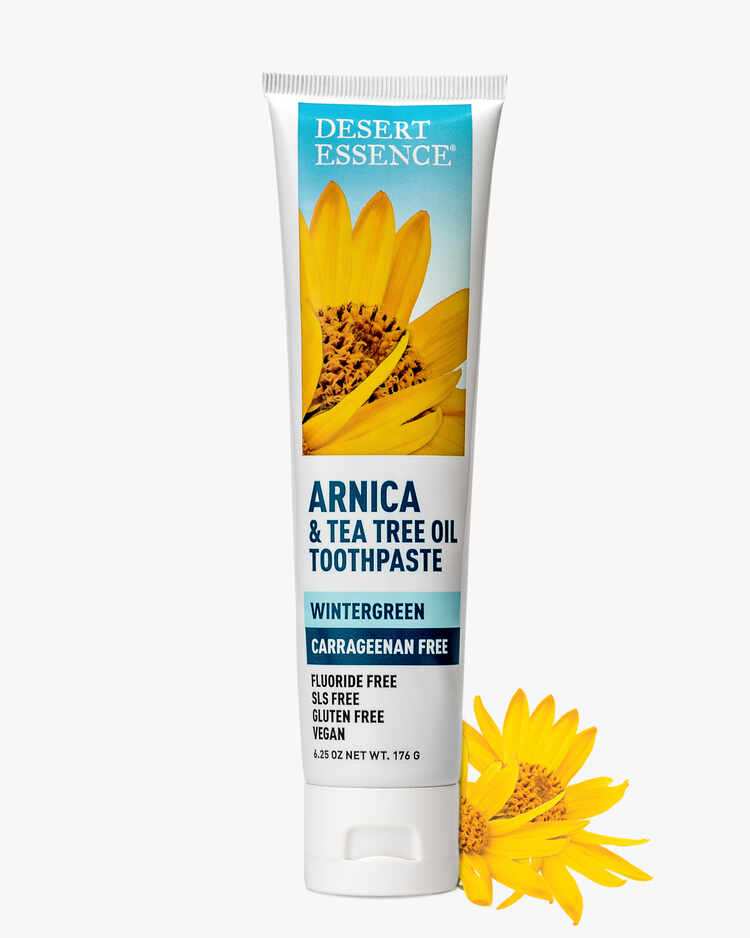 6.25 oz. tube of the Arnica and Tea Tree Oil Toothpaste Wintergreen next to flowers by Desert Essence.