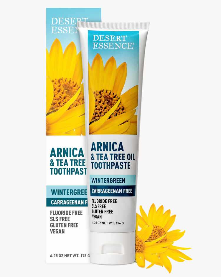 6.25 oz. tube of the Arnica and Tea Tree Oil Toothpaste Wintergreen next to flowers and packaging by Desert Essence.