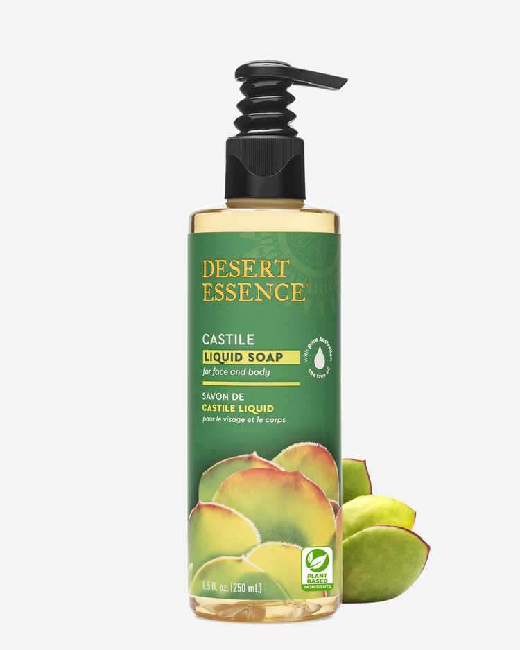 Pump bottle of Desert Essence Castile Liquid Soap for face and body, 8.5 fl. oz with plant next to it. 